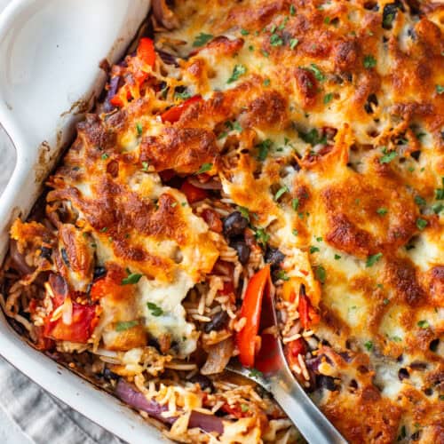 A large spoon taking a scoop of cheesy baked fajita rice.