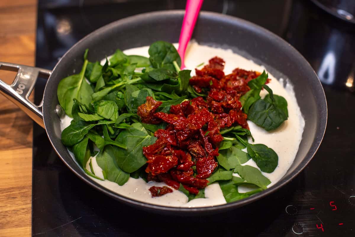 Creamy tofu sauce in a pan topped with chopped spinach and sun-dried tomatoes.