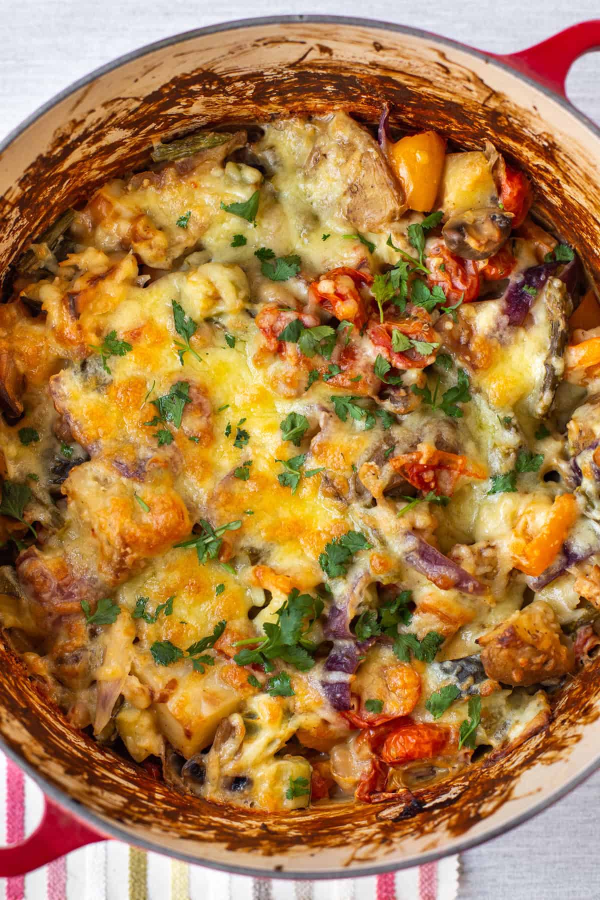 Overhead shot of cheesy vegetable potato bake topped with fresh herbs.