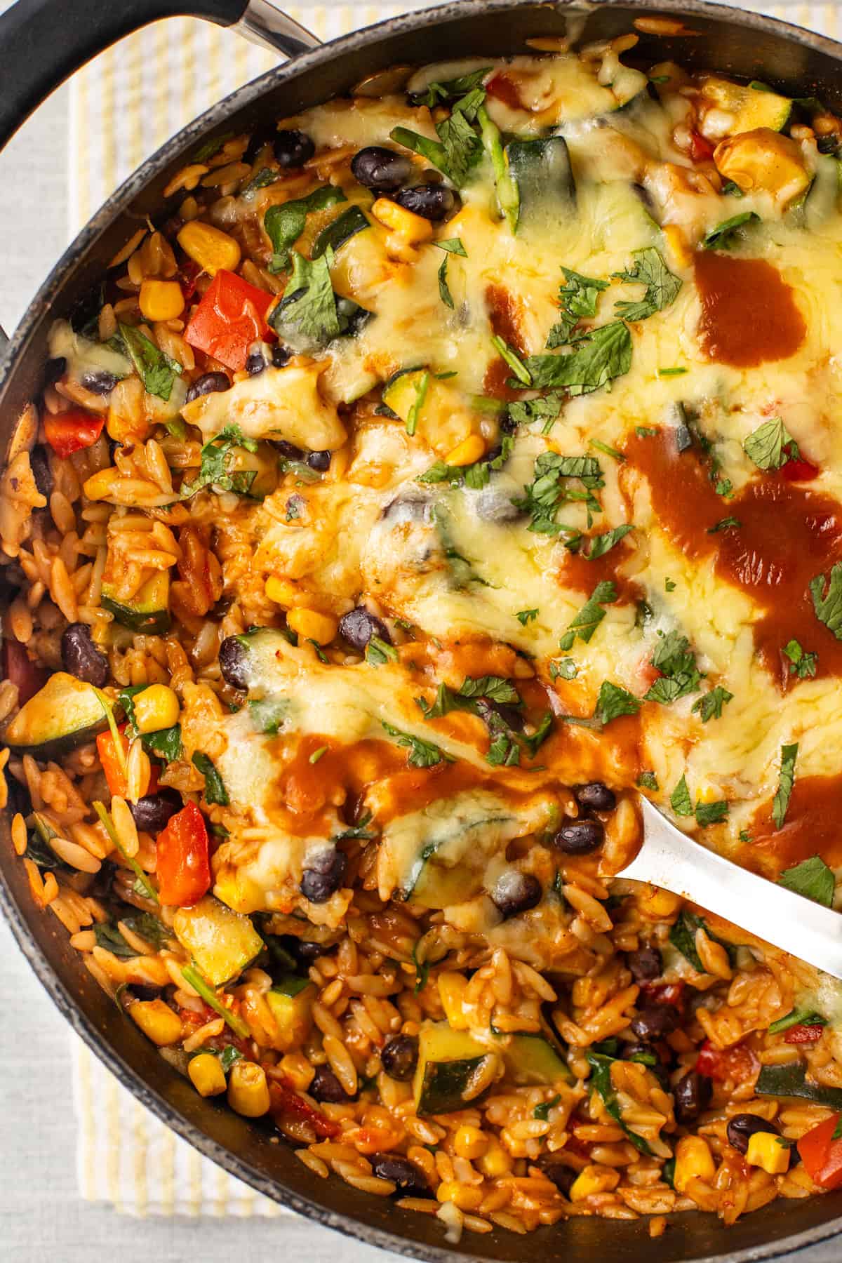 A large spoon taking a scoop from a pan of cheesy enchilada orzo.